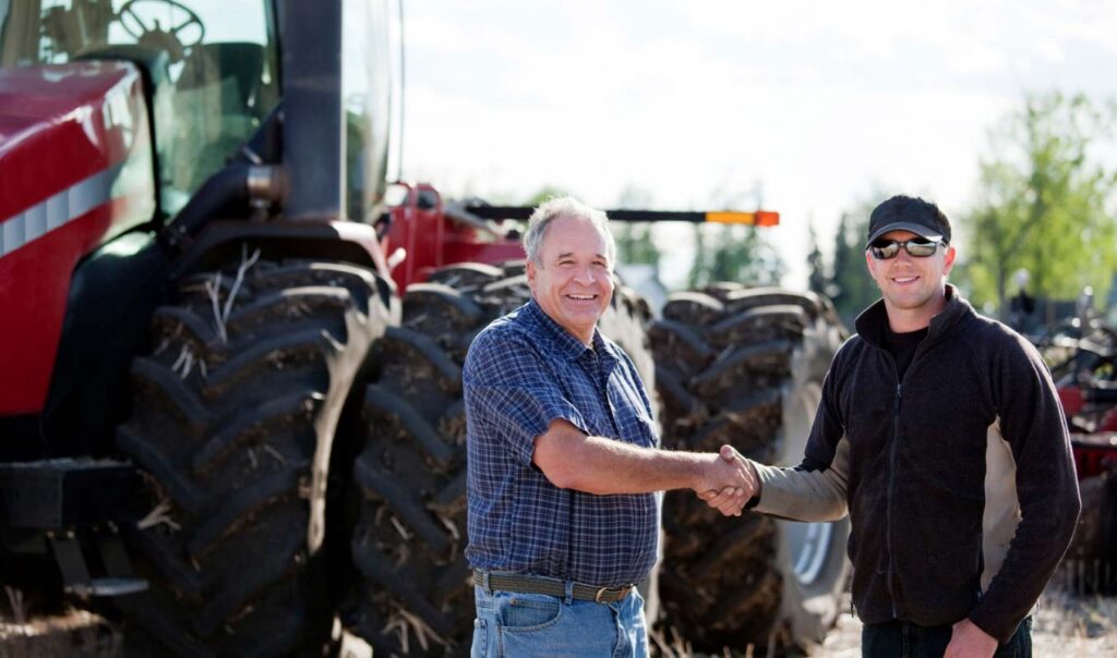 two men shaking hands in front of a tractor