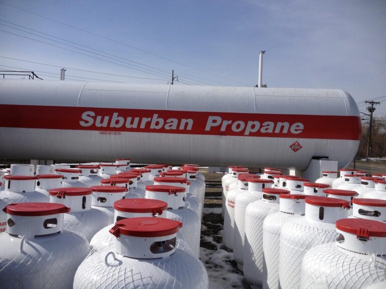 Rows of portable propane tanks sitting in front of a fixed propane tank