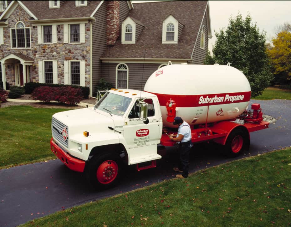 A Suburban Propane technician making a propane delivery to a brick home.